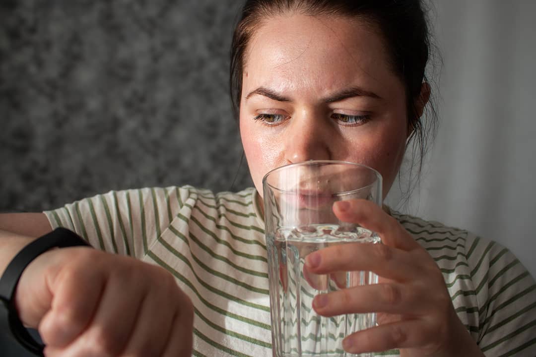 A person checking her heart rate and pulse from a smart watch, while drinking a glass of water.